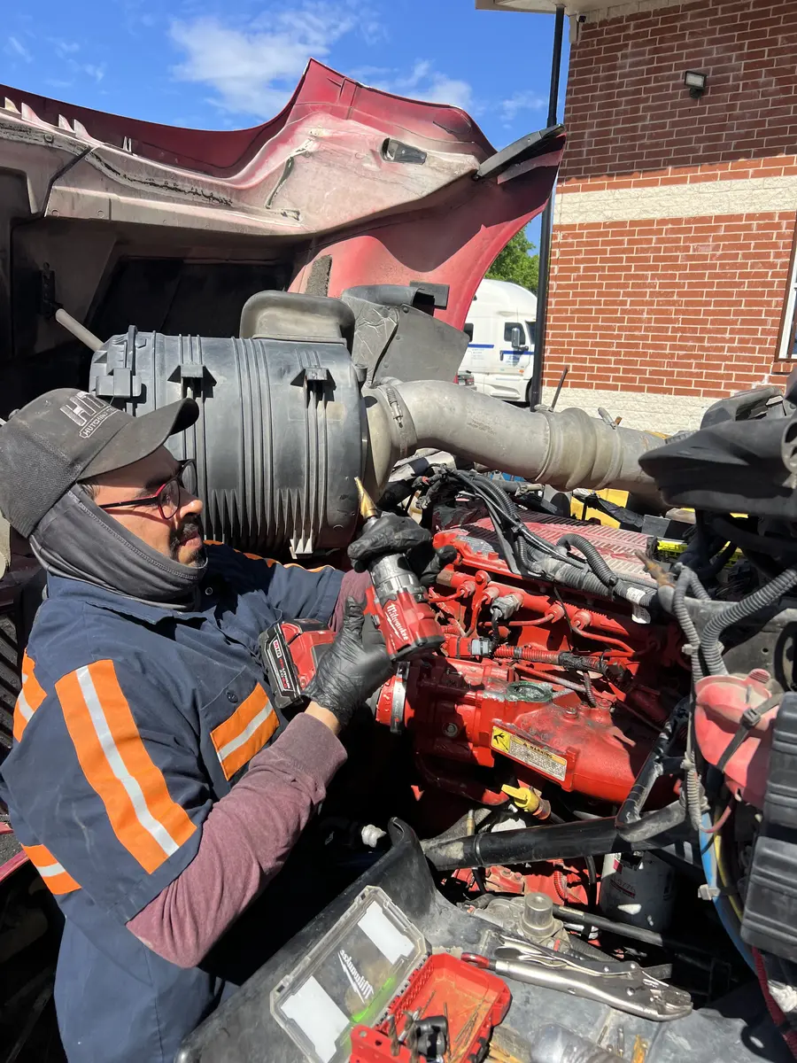 Real Lonestar Diesel technician working inside the open engine compartment of a red commercial truck.